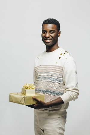 Smiling Black man holding two presents wrapped in gold paper