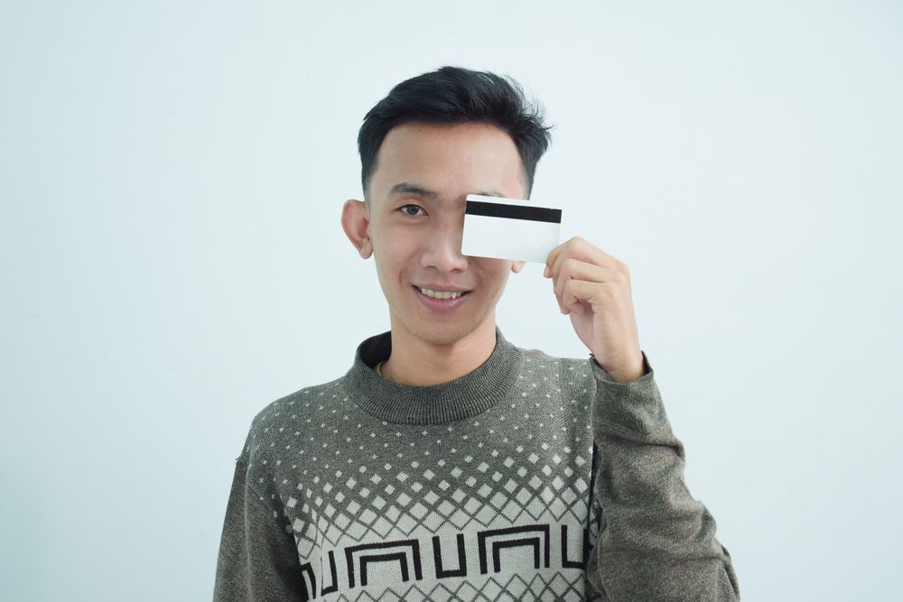 Playful Asian young men in sweater and holding blank credit card