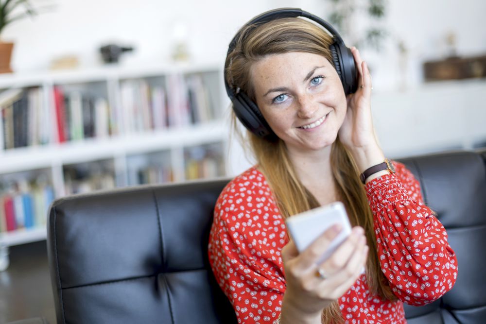 Smiling blonde woman using a smartphone while relaxing on leather sofa