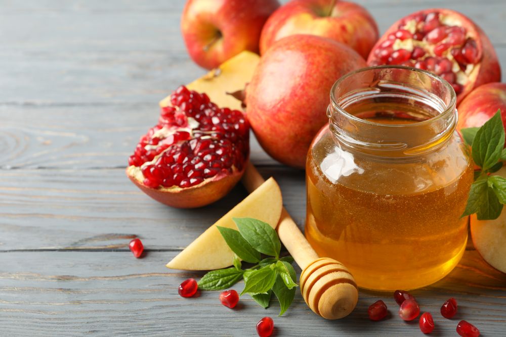 Honey pot surrounded by slices apples and pomegranate on grey table with text for space