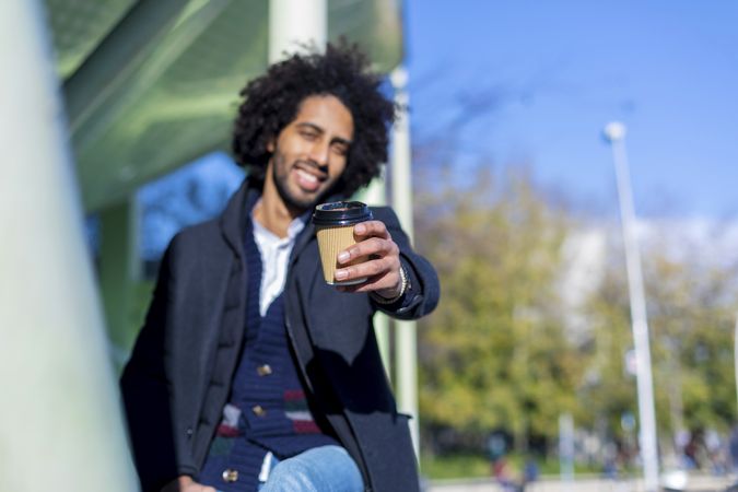 Smiling Black man in jacket holding out warm beverage to camera