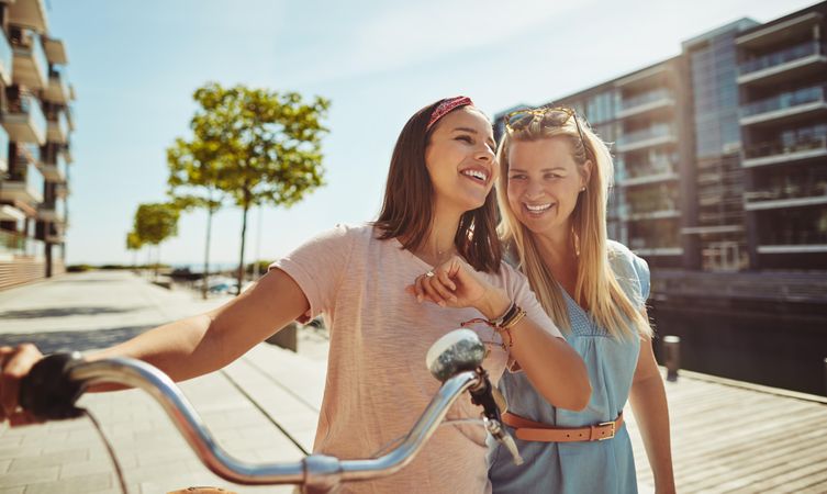Two friends with walking with bike next to river, copy space