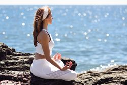 Side view of female stretching her back in lotus pose on rocky beach