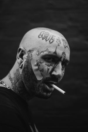 Side portrait of  bald man with face tattoos smoking cigarette with band-aid on face