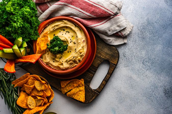 Top view of hummus dish on cutting board with chips and fresh veggies with copy space