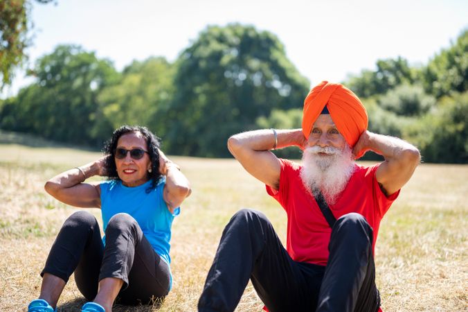 Older Sikh couple doing sit ups in park