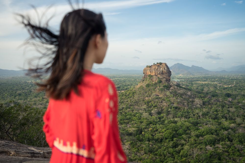Tourist against solitary rock in middle of green forested plain under clear sky in summer