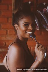 Smiling woman eating with spoon standing in the kitchen bYMeXb