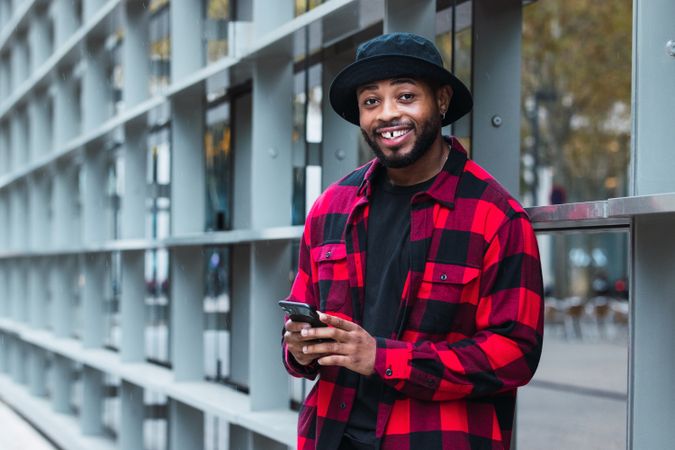 Cheerful Black male with smartphone in contemporary building