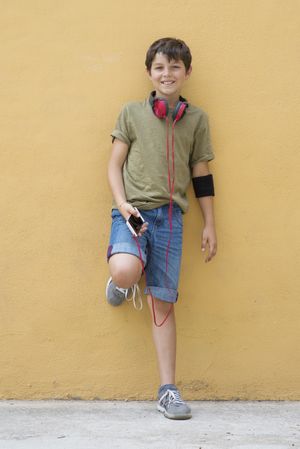 Young teen boy leaning on a yellow wall with headphones on neck