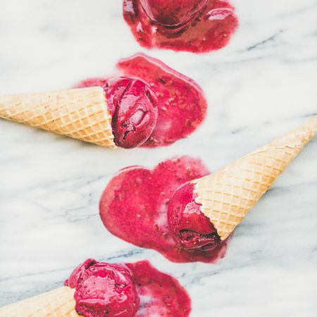 Cones of dark berry ice cream melting on marble slab, square crop