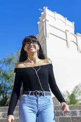Smiling woman wearing earphones spending free time outdoors standing listening to music looking up