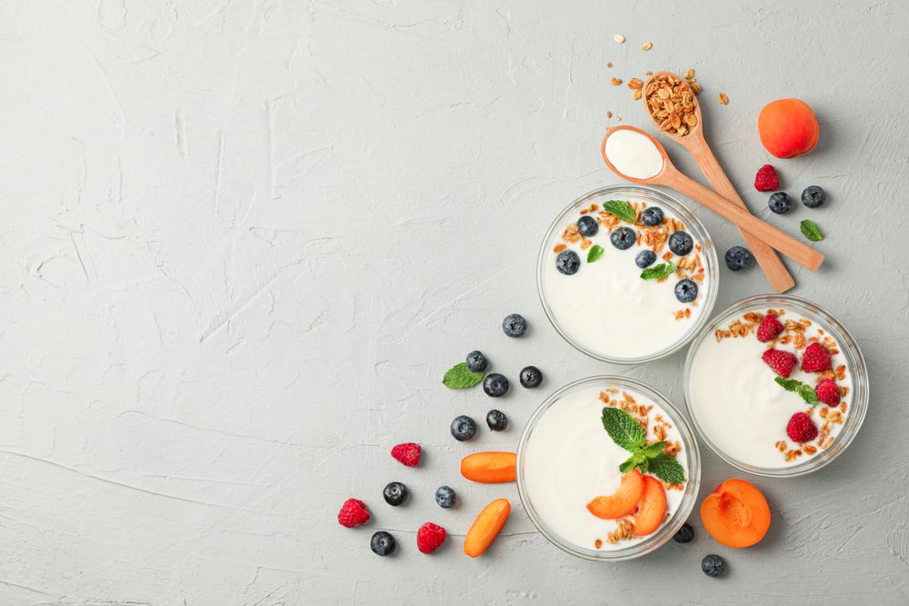 Flat lay composition with yogurt desserts and fruits on grey cement background