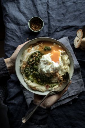 Person holding bowl with cauliflower puree with pesto and eggs