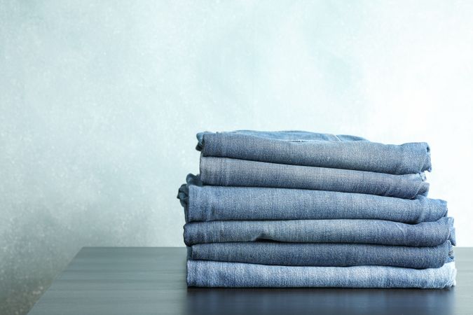 Stack of jeans pants on table, space for text