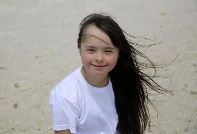 Happy girl with long dark hair on the beach smiling and looking at camera