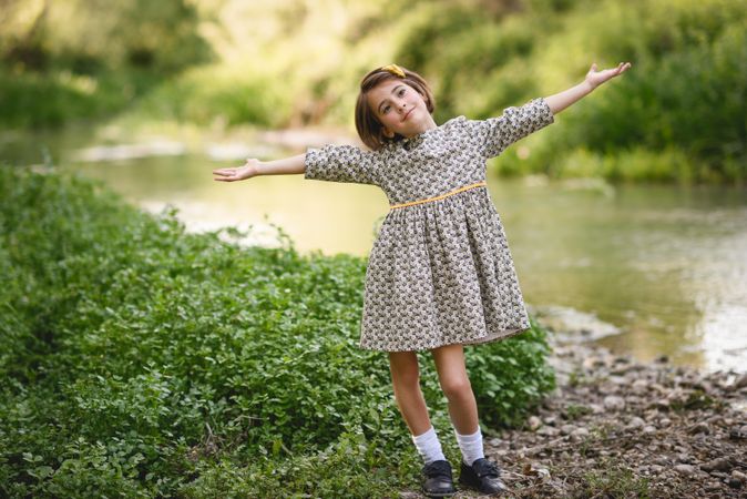 Child standing by river with her arms open
