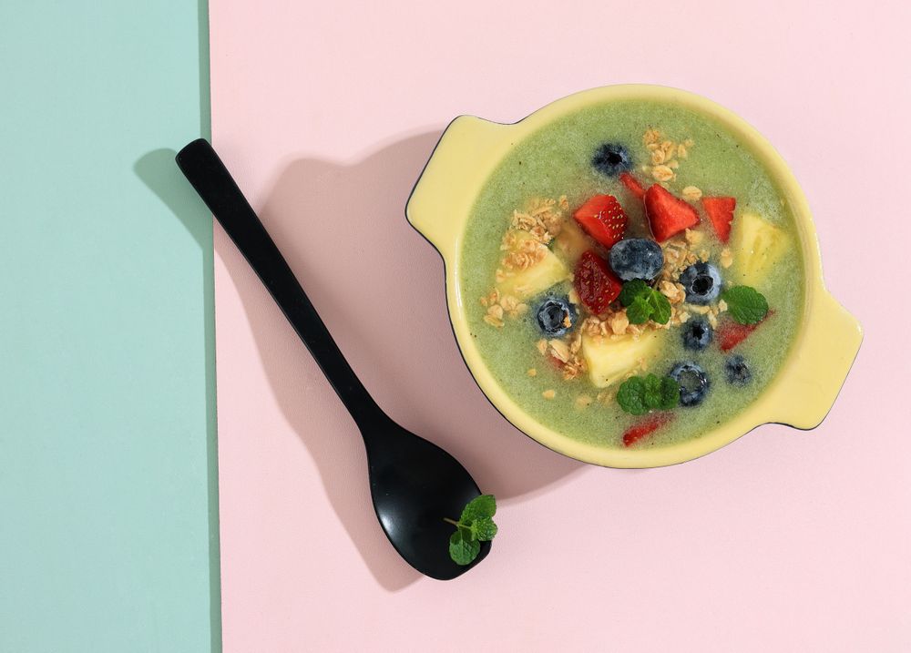 Top view of smoothie with fresh fruit and granola on duo tone background