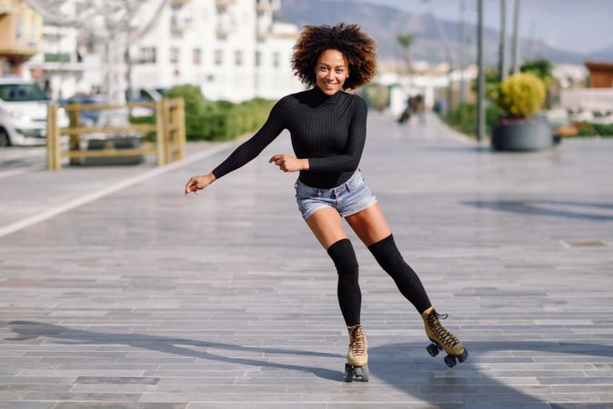 Happy woman with afro roller skating outside on a path
