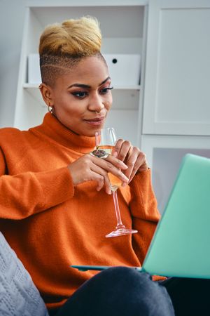 Black woman with a champagne flute while watching something on her laptop