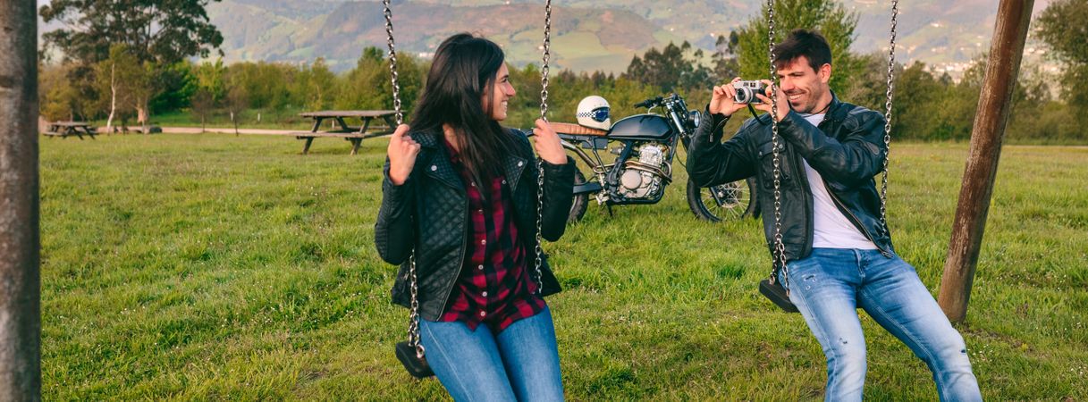 Young man taking a picture of his girlfriend on the swings