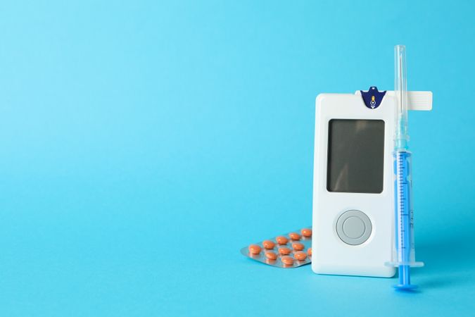 Blood glucose meter, syringe and pills on blue background