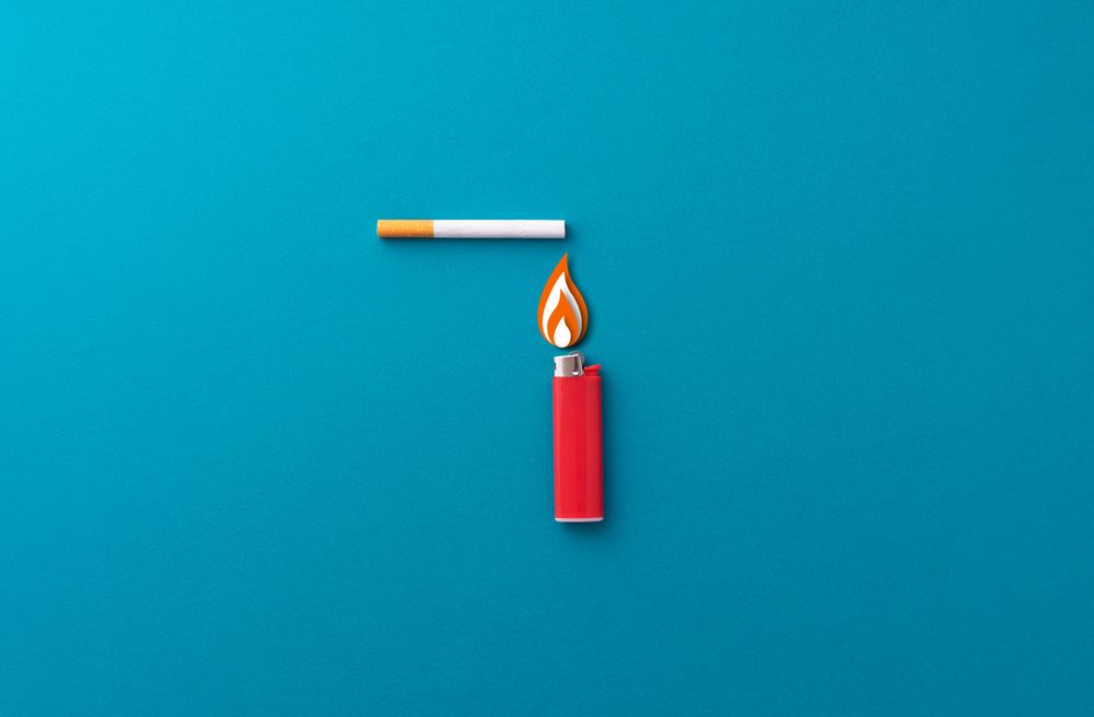 One red lighter and one cigarette on blue background