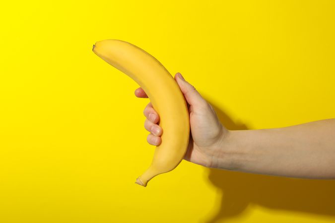 Female hand holds banana on yellow background. Fresh fruit