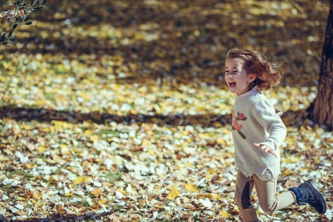 Playful child running in park of colorful fall leaves with her arms open