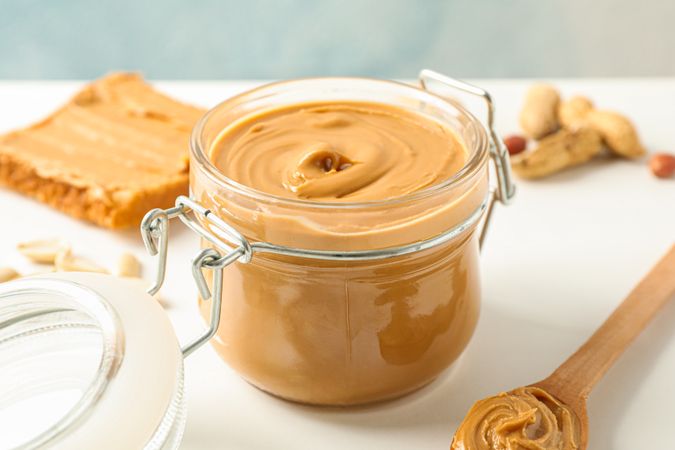 Composition with peanut butter sandwich, glass jar, peanut and spoon on table against light background, space for text and closeup