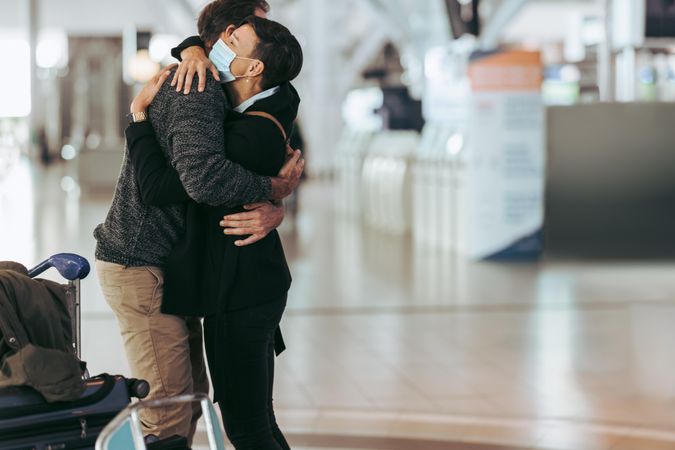 Woman in face mask hugging man at airport arrival gate