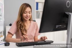 Happy Asian woman sitting in office and concentrating on typing on keyboard bY9k6b