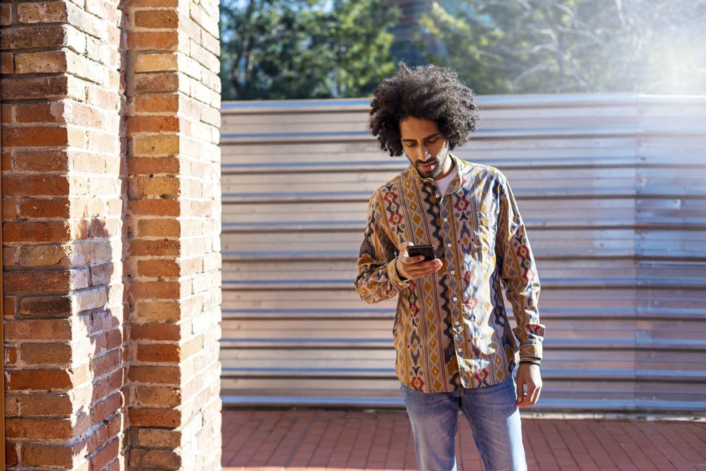 Front view of a man using a mobile phone while standing outdoors on a sunny day