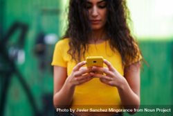 Woman with curly hair in yellow t-shirt and jeans texting on phone 5owng5