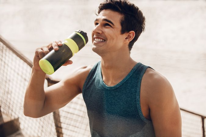 Happy young man drinking water after workout outdoors
