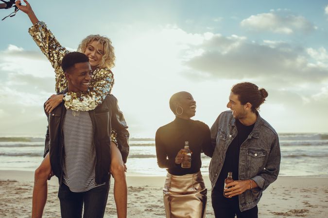 Two happy young men with girlfriends having fun at a beach during sunset