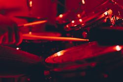 Anonymous man with drumsticks playing on drums in redness