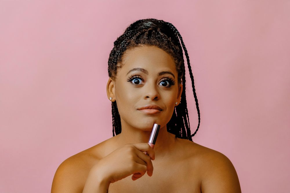 Surprised Black woman holding lip gloss while looking up