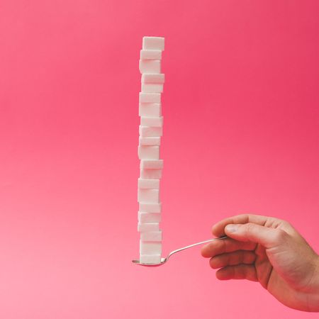 Sugar cubes stacked on spoon on pink background