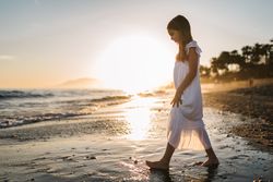 Adorable girl walking on seaside at sunset