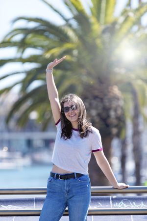 Joyous woman wearing clothes standing outdoors in the street while checking phone on a sunny day