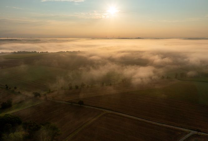 Drone aerial view with golden light illuminating foggy agricultural fields and rolling hills