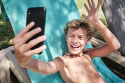 Cheerful boy sitting and taking selfie on poolside