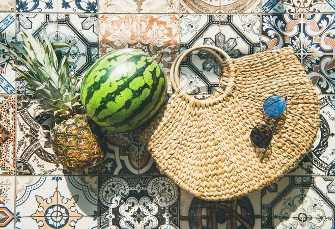 Thatched bag on pattered tiles with sunglasses, watermelon, horizontal composition