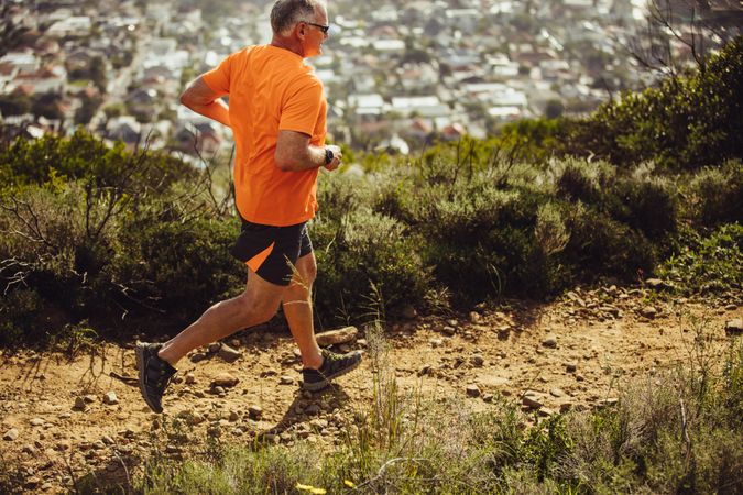 Side view of a mature man trail running on a hill