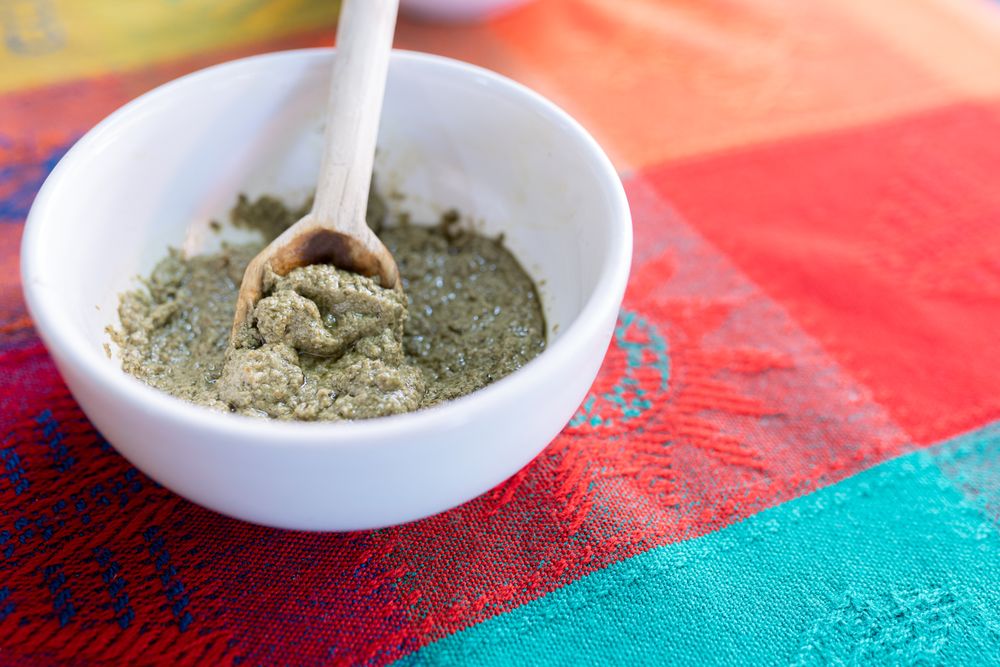 A bowl of green mole sauce with a wooden spoon on top of a colorful traditional tablecloth
