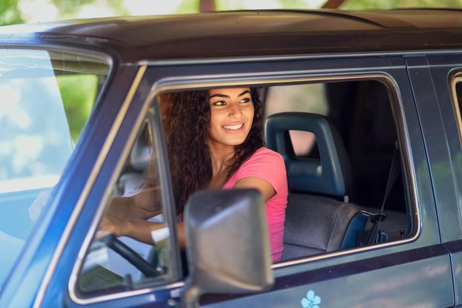 Female in pink t-shirt with curly hair sitting up in driver’s side of vehicle