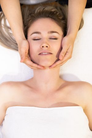 Young woman with masseuse working on her face and neck in a spa