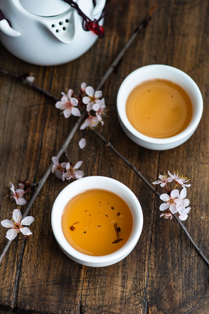 Top view of cups of green tea with floral petals on wooden board