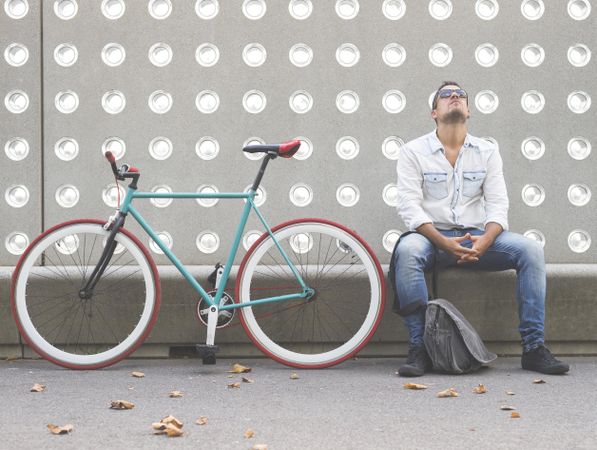 Exasperated male sitting with bike parked in front of patterned cement wall